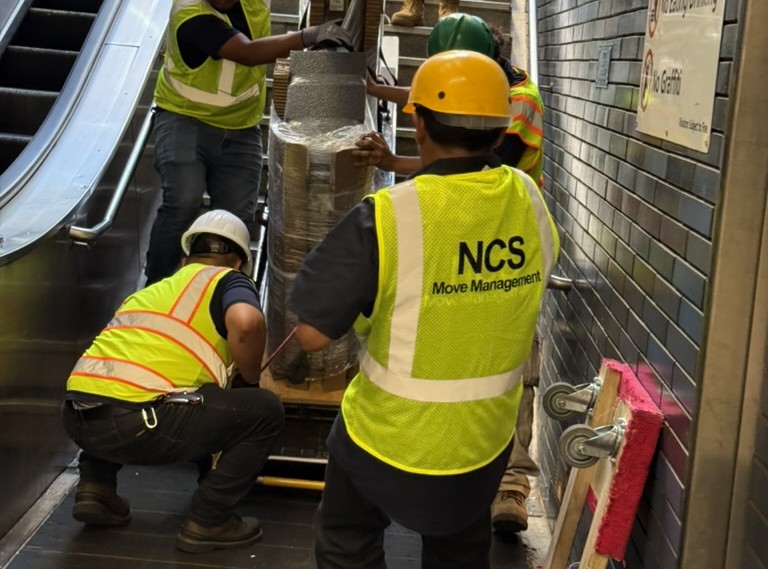 NCS crew rigging equipment down transit station stairs in hard hats and high visibility vests
